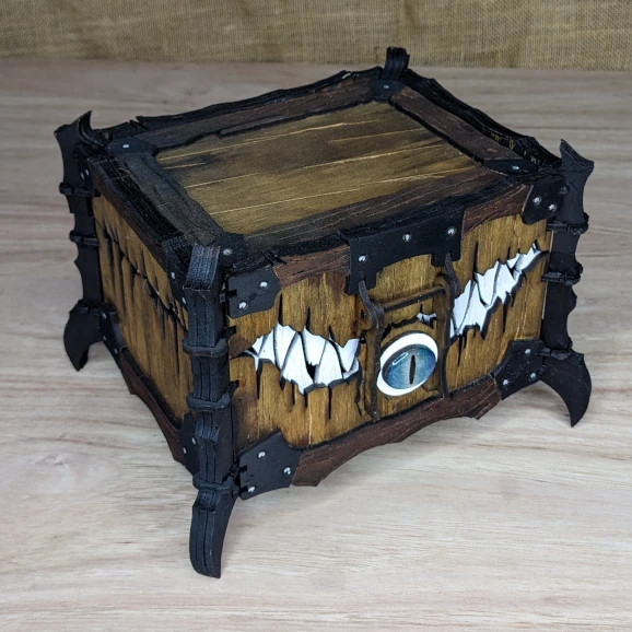 Handcrafted wooden one-eyed mimic chest with latch detail, inspired by fantasy and tabletop role-playing games.